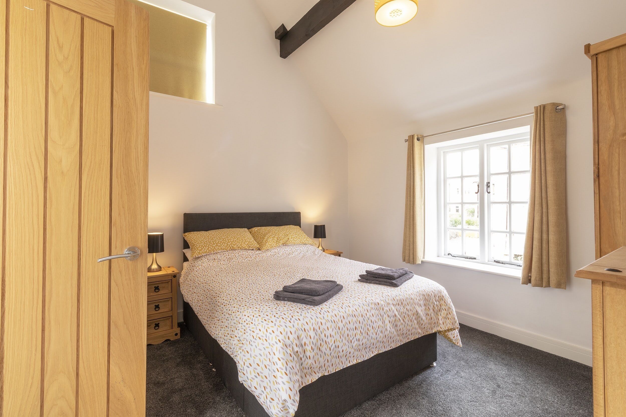 A bedroom with a bed, bedside tables, a wardrobe, and a window with curtains.