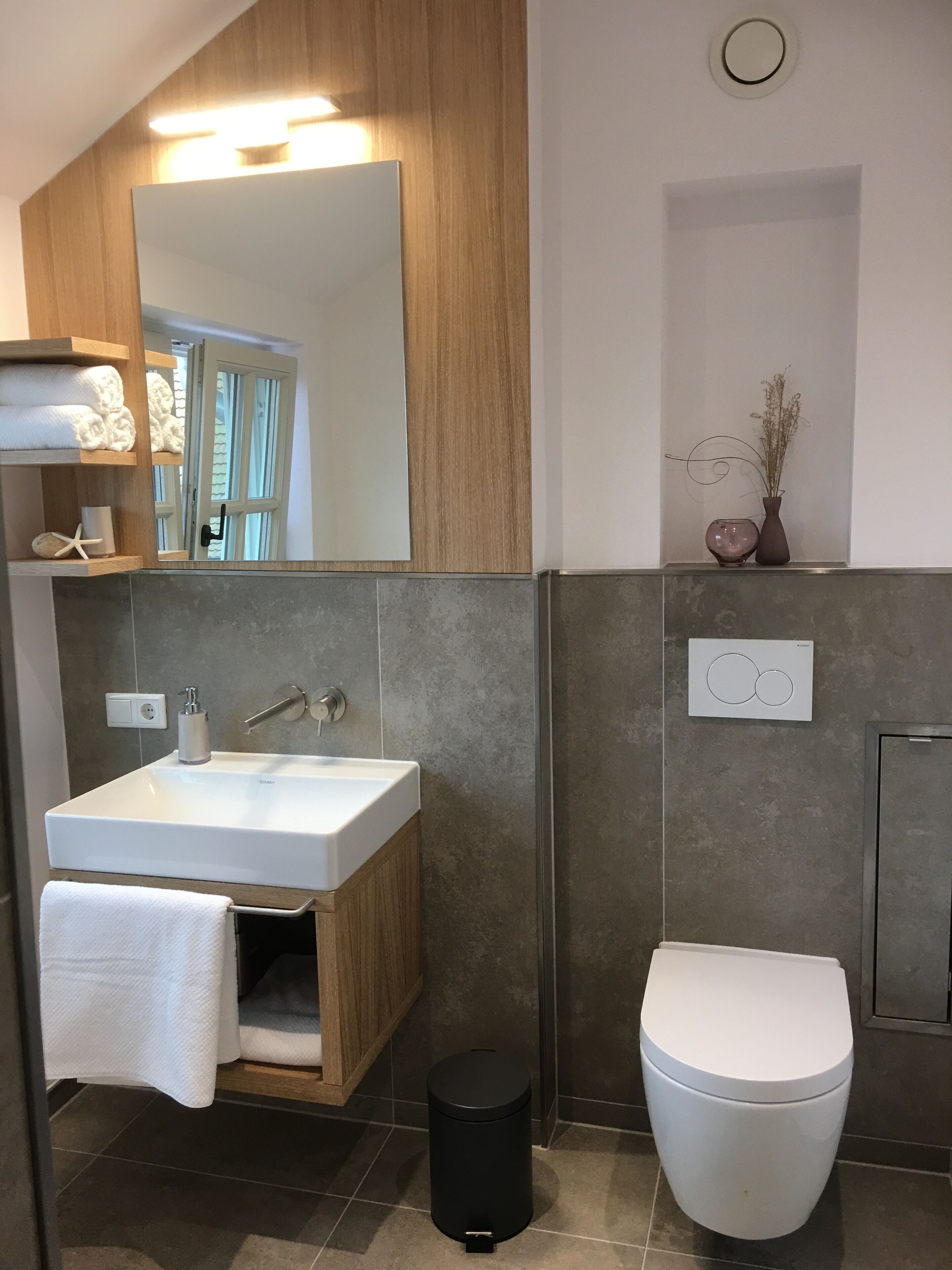 A modern bathroom with a wooden vanity, white sink, and toilet.