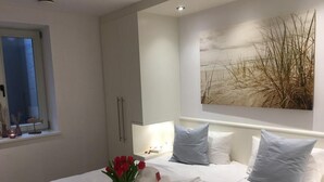 Ein Hotelzimmer mit einem großen Bett, weißen Leinen, einer Vase mit roten Blumen und Wandbildern zum Thema Strand.