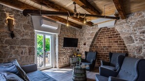 A cozy room with a stone wall, a wooden ceiling, a large window, a flat-screen TV, and a rustic barrel coffee table. - Stone house Katarina with swimming pool, only 50 meters from the Sea (Klimno (Krk))