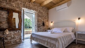 A bedroom with a stone wall, wooden floor, a bed with white bedding, a nightstand, and a mirror. - Stone house Katarina with swimming pool, only 50 meters from the Sea (Klimno (Krk))