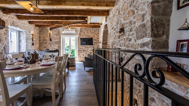 A rustic dining area with stone walls, wooden beams, and a long table set for a meal. - Stone house Katarina with swimming pool, only 50 meters from the Sea (Klimno (Krk))