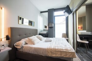 A modern hotel room with a large bed, bedside tables, a flat-screen TV, a mirror, and a view of the outdoors. - Dingdong Nuns (Valencia)