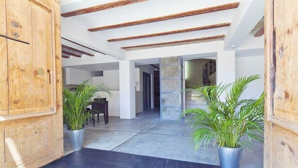 A spacious interior with a high ceiling, exposed wooden beams, and a central open area with a dining table and chairs. There are potted plants on either side of the entrance. - Dingdong Nuns (Valencia)