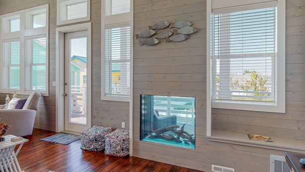 A room with wooden floors, a fireplace, and large windows with blinds.