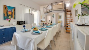 A dining area with a long table set for a meal, a kitchen area with a refrigerator, and a staircase leading to an upper level. - Villa Dada with pool, Seaview and playroom (Linardići (Krk))
