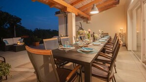 An outdoor dining area with a long wooden table set for a meal, surrounded by wicker chairs. - Villa Dada with pool, Seaview and playroom (Linardići (Krk))