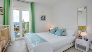 A bedroom with a bed, nightstand, and a view of a pool and greenery. - Villa Dada with pool, Seaview and playroom (Linardići (Krk))