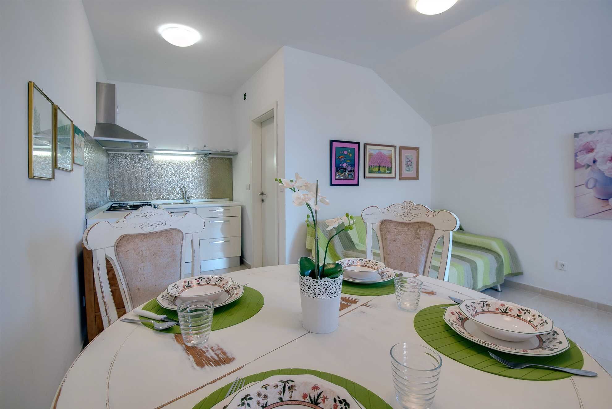 A dining area with a table set for four, a kitchen in the background, and artwork on the walls.