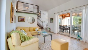 A spacious living room with a beige sofa, a glass coffee table, and a yellow ottoman. A staircase leads to a balcony with outdoor seating. - Villa Dada with pool, Seaview and playroom (Linardići (Krk))