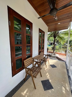 A covered outdoor seating area with a wooden bench and table, large windows, and a ceiling fan. - Airis Sanctuary Resort (Langkawi)