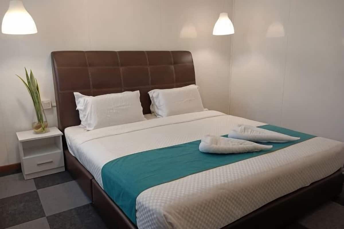 Ein Hotelzimmer mit einem Bett, weißen Kissen, einer türkisblauen Bettdecke, einem braunen Kopfteil und zwei Nachttischlampen.