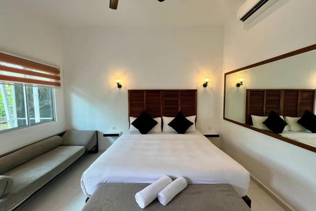 A hotel room with a large bed, a bench, and a large mirror.