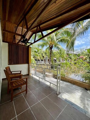 A covered balcony with a wooden bench, a metal railing, and a view of palm trees and buildings. - Airis Sanctuary Resort (Langkawi)
