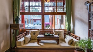 A traditional wooden sofa with cushions, a small table with tea set, and a view of a courtyard with buildings and greenery.