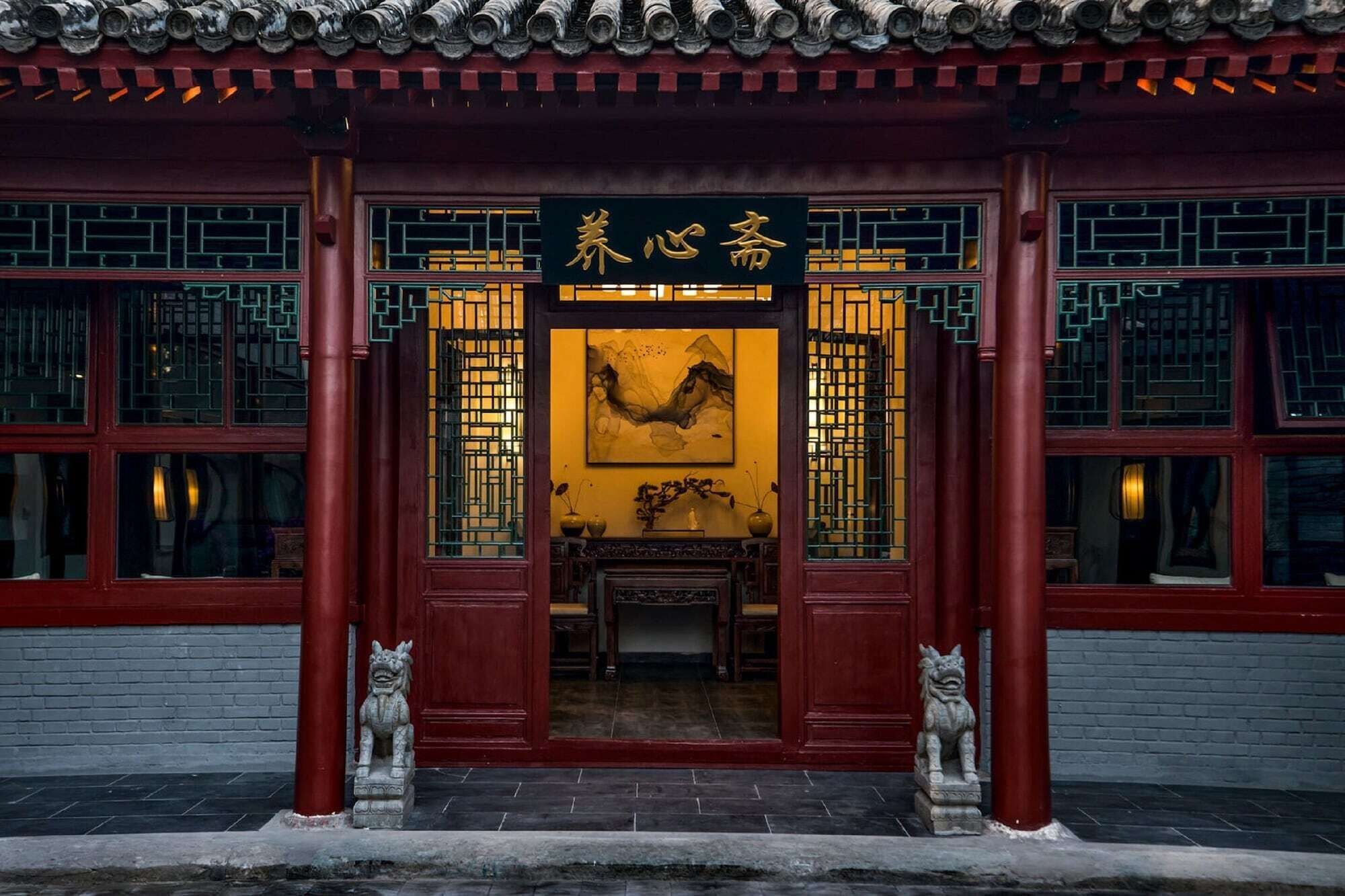 A traditional Chinese building with a red facade, a sign with Chinese characters, and a lion statue at the entrance.