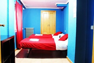 Una habitación con dos camas, una puerta de madera, un radiador y una cortina roja.
