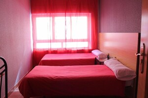 A small room with two beds, a window with sheer curtains, and a wooden headboard.