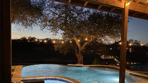 A hot tub area with a tree and string lights, surrounded by a covered patio.