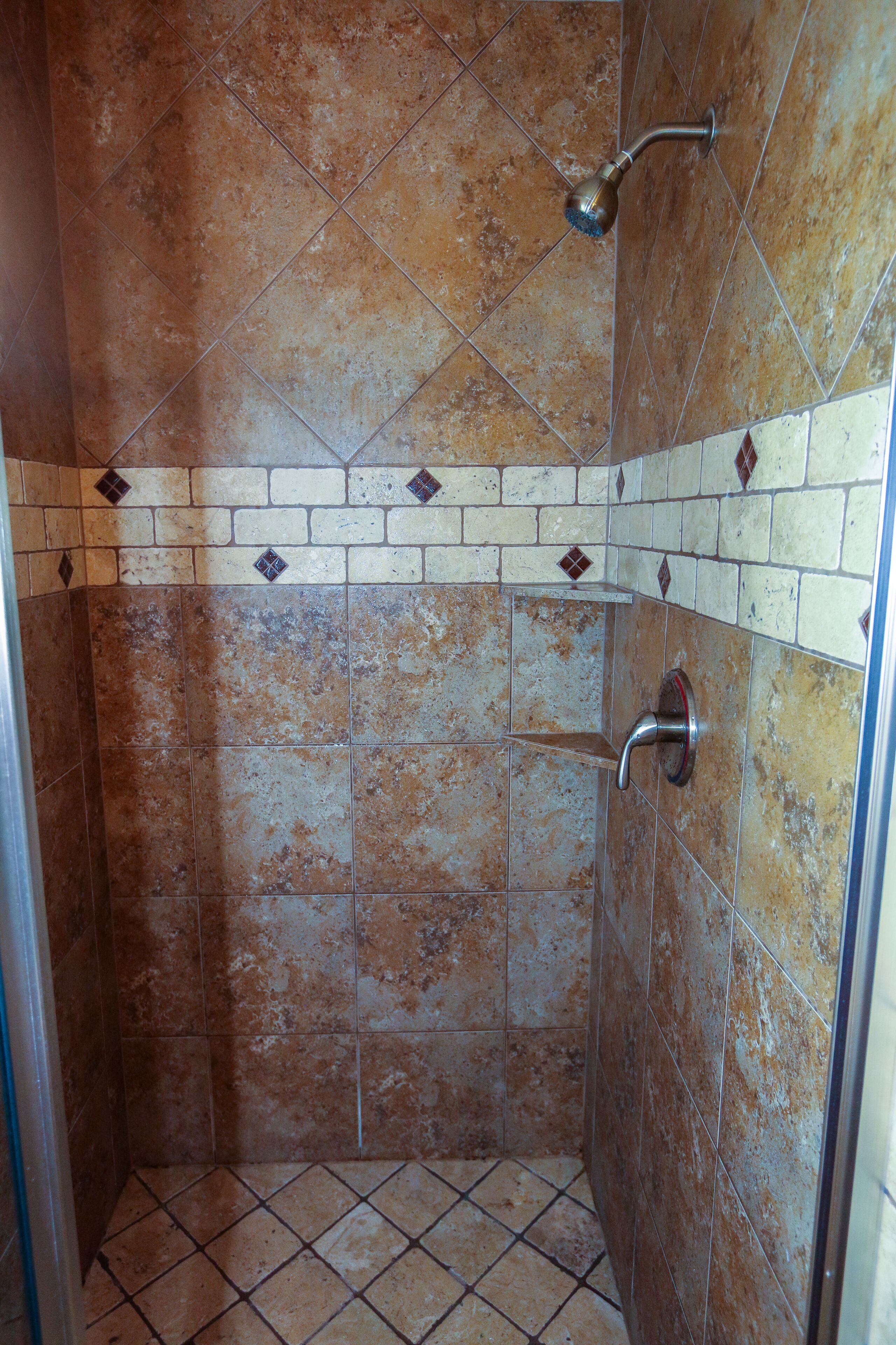 A shower with a handheld showerhead, a wall-mounted towel rack, and a tiled floor.