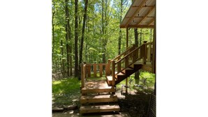 Una scala in legno conduce a una zona riparata, dotata di ringhiera metallica, immersa in una zona boschiva.