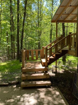 A wooden staircase leading to a covered area with a metal railing, surrounded by a forested area.