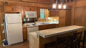 Una cucina con mobili in legno, frigorifero, fornello, microonde e una zona bar con sedie.
