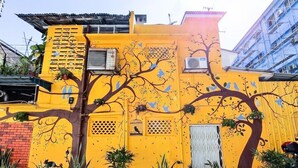 A yellow building with a tree mural, potted plants, and a white door. - The Yard Boutique Hotel (Kuala Lumpur)