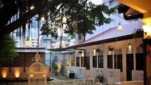 An outdoor dining area with tables and chairs, a hanging light fixture, and a tree in the background. - The Yard Boutique Hotel (Kuala Lumpur)
