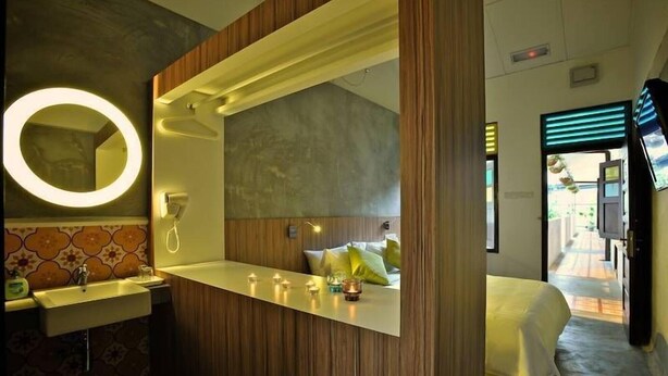 A hotel room with a wooden vanity, a round mirror, a bed with a green pillow, and a view of the outside balcony. - The Yard Boutique Hotel (Kuala Lumpur)