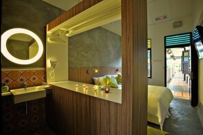 A hotel room with a wooden vanity, a round mirror, a bed with a green pillow, and a view of the outside balcony. - The Yard Boutique Hotel (Kuala Lumpur)