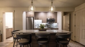 Une cuisine moderne dotée d’un îlot central, de tabourets de bar, d’appareils électroménagers en acier inoxydable et de luminaires suspendus.