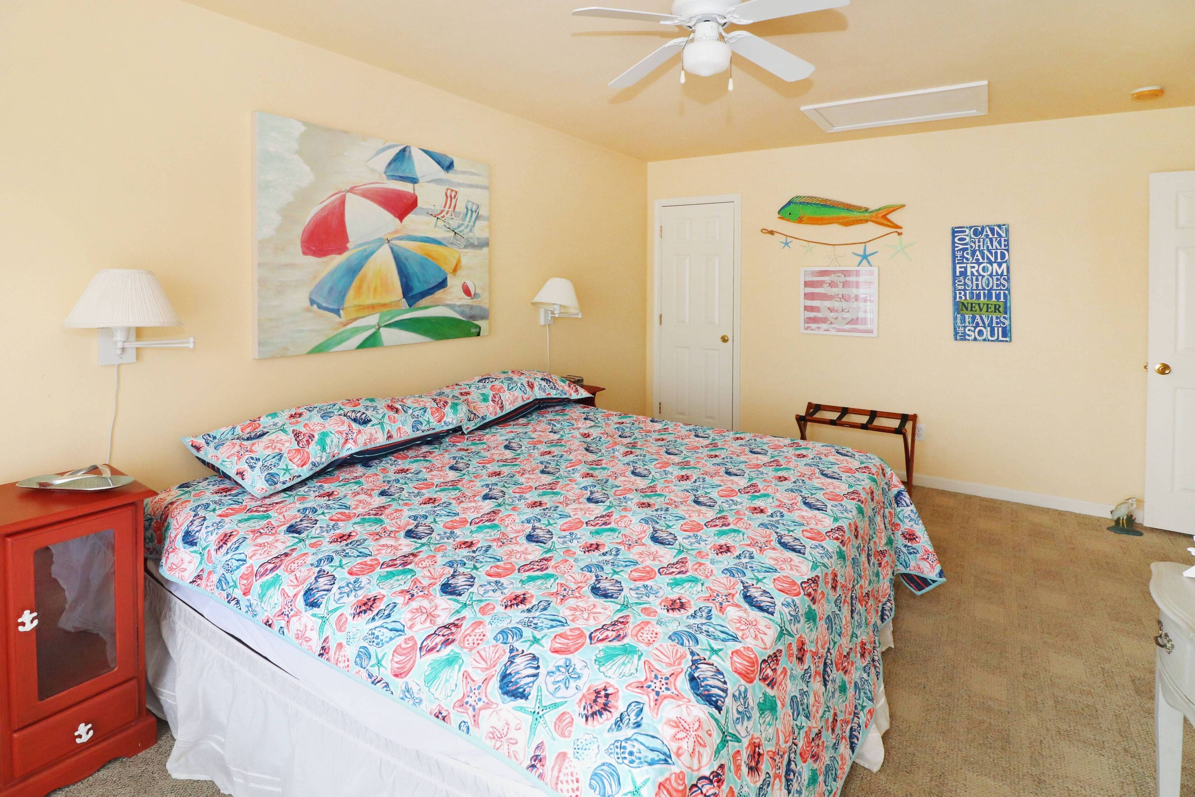 A bedroom with a bed, a nightstand, a ceiling fan, a door, and wall decorations.