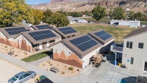 A building with multiple solar panels on the roof, surrounded by a parking area and a mountainous landscape in the background.