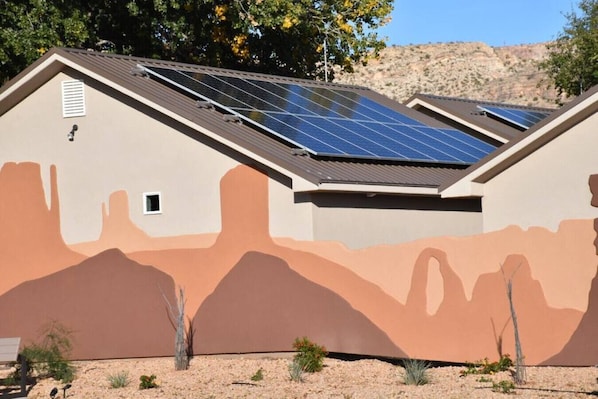 Un edificio con un mural de temática desértica, paneles solares en el techo y una ventana pequeña.