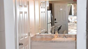 Un pasillo que conduce a un baño con lavamanos doble, un espejo y una puerta.