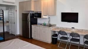 Cocina compacta con refrigerador, microondas y pileta, junto con un televisor instalado en la pared.
