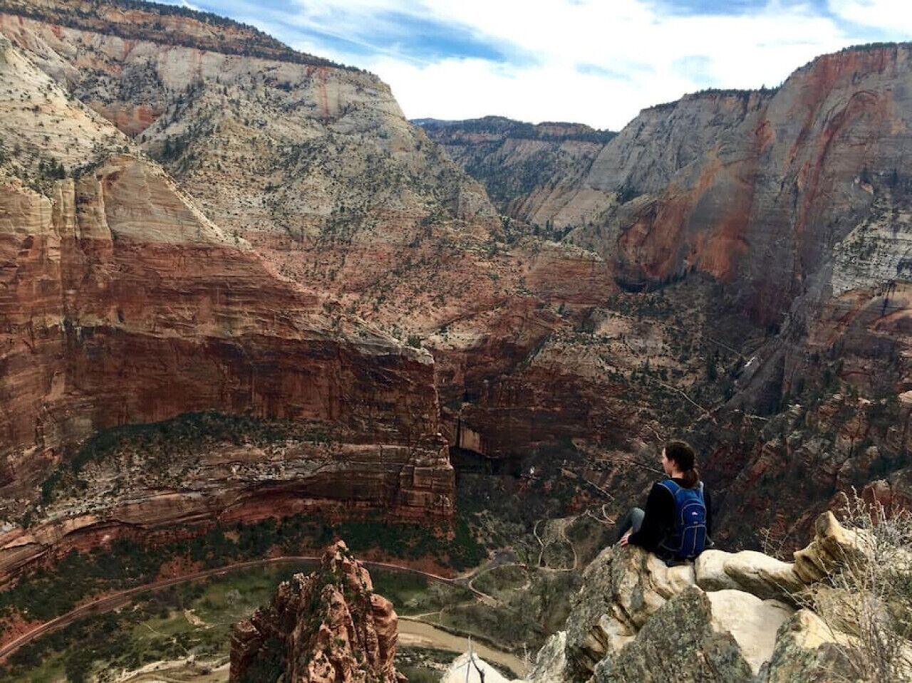 Una persona sentada sobre una roca con vistas a un cañón y formaciones rocosas estratificadas.