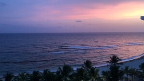 Vista de playa con palmeras y olas del océano al atardecer.