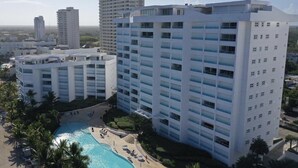 Un hotel moderno con varios pisos, un patio central con piscina y vistas del paisaje urbano circundante.