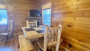 Interior de una cabaña de madera con una mesa de comedor, bancos y un televisor.