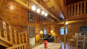 Interior de una cabaña de madera con cocina, escalera de madera y una mesa de comedor.