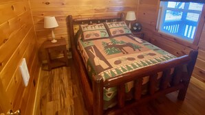 Una habitación de cabaña de madera con cama, dos lámparas de noche, una ventana con persianas y una lámpara de techo.