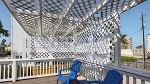 Una terraza techada al aire libre con estructura de celosía, sillas Adirondack azules y una pequeña mesa.