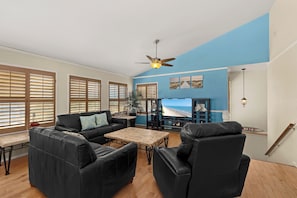 A living room with a sofa, chairs, a coffee table, and a view of the beach through large windows.