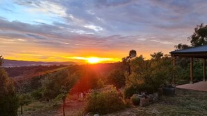A sunset view from a covered outdoor area with a brick building and surrounding vegetation. - Dog Friendly Snowy Mountains Cottage on Acres (Berridale)