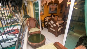 Un balcon agrémenté de meubles en osier, d’une table en verre et offrant une vue sur les voitures garées.