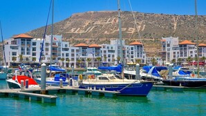 A marina with boats docked, a mountainous backdrop, and buildings with red roofs. - Residence Marina Agadir 5210 (Agadir)