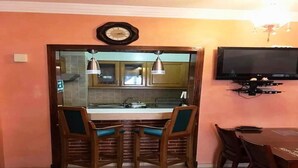 A kitchen with a wooden counter, two chairs with teal cushions, a clock, and a TV mounted on the wall. - Residence Marina Agadir 5210 (Agadir)