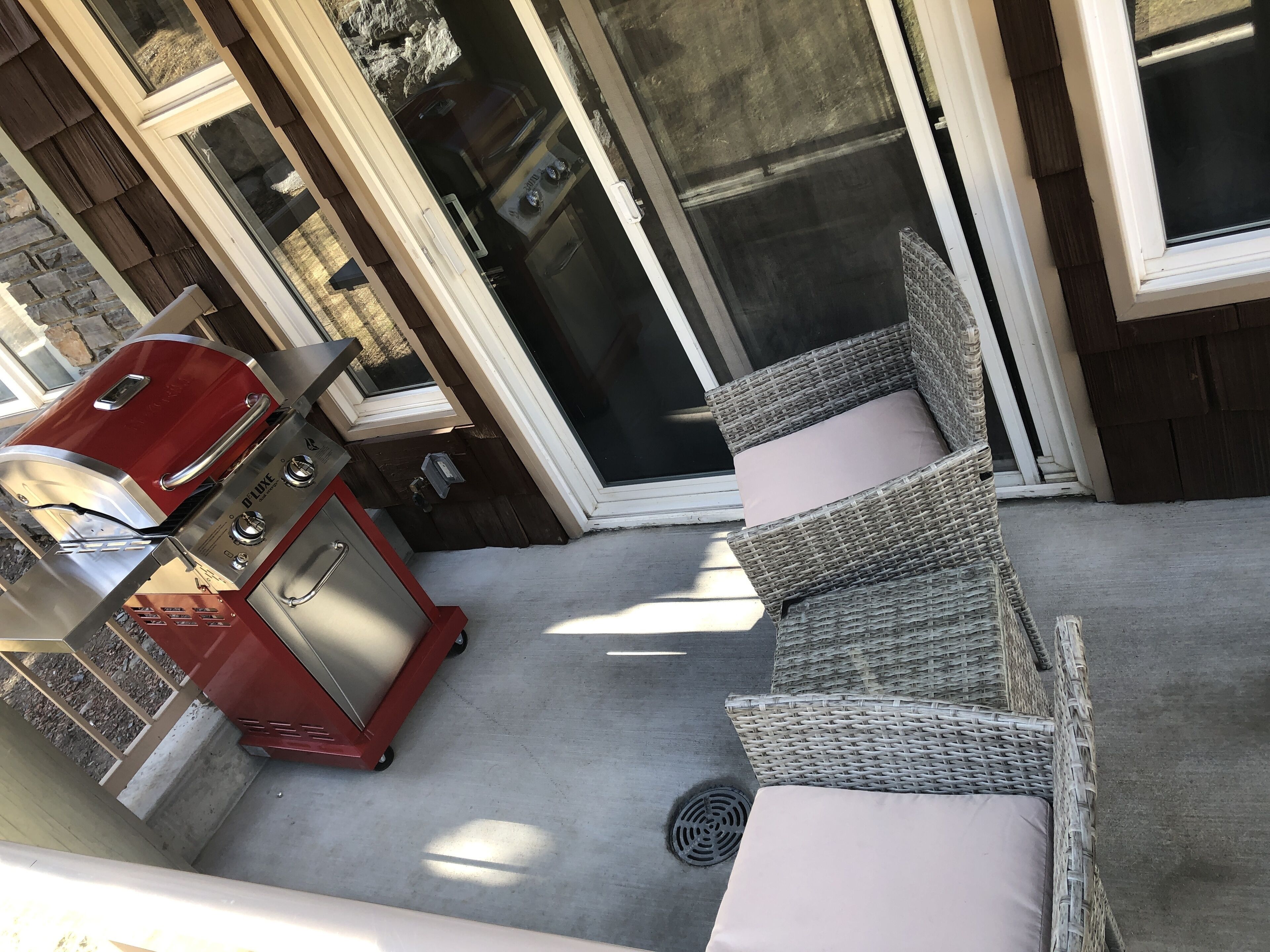 A patio area with a red grill, wicker furniture, and a sliding glass door.